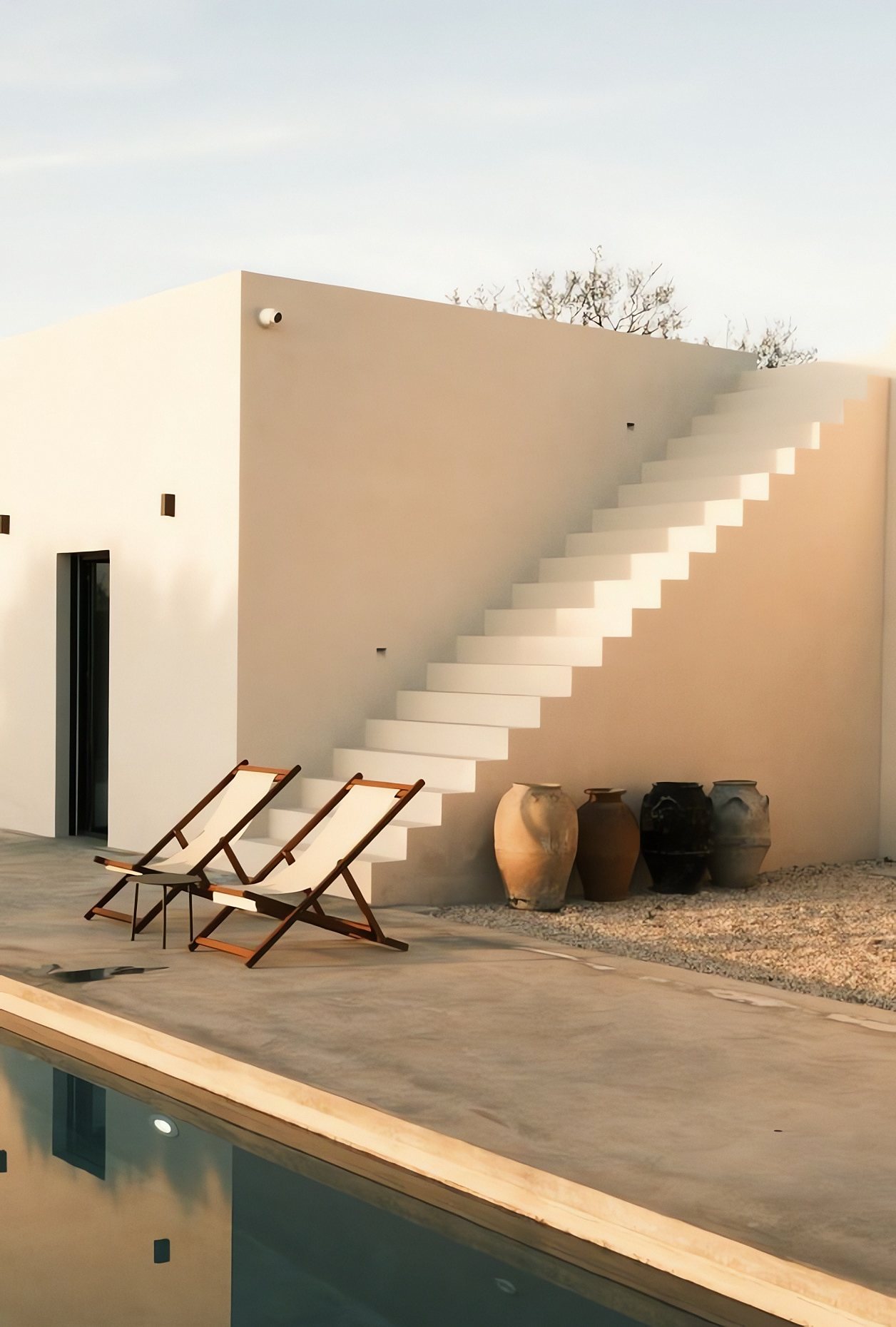 Casa encalada con escalera exterior, tumbonas y piscina